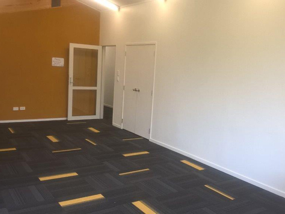 Empty room with vaulted timber-beam ceiling, patterned carpet, and orange accent wall