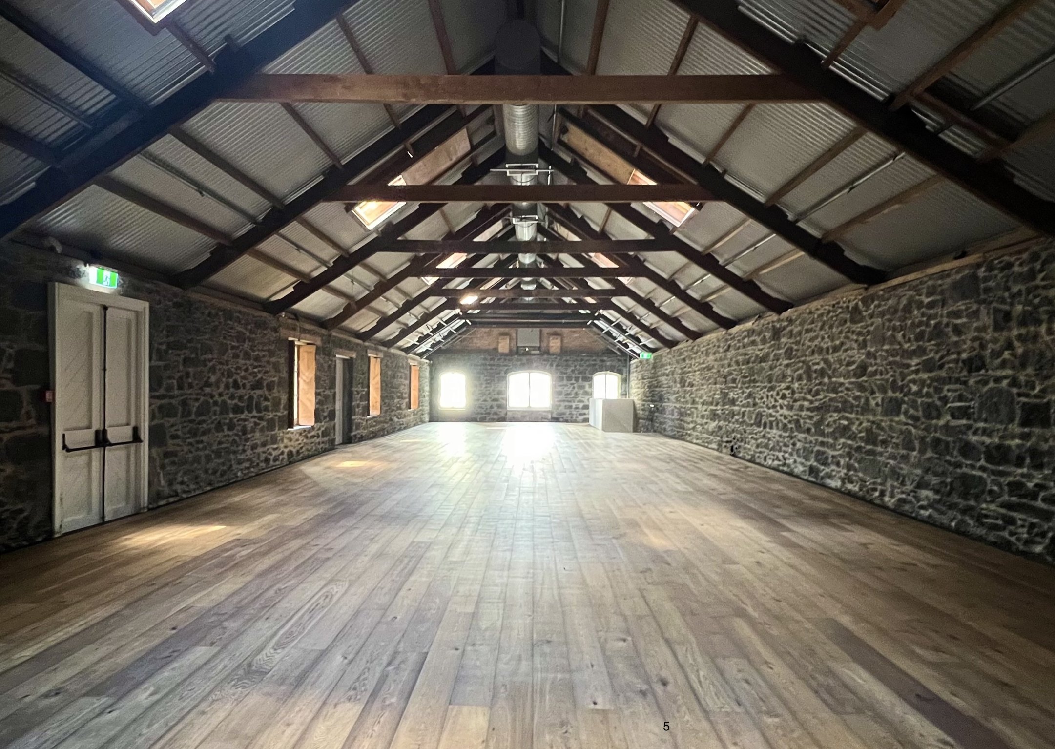 Empty stone-walled barn with exposed rafters and timber floor
