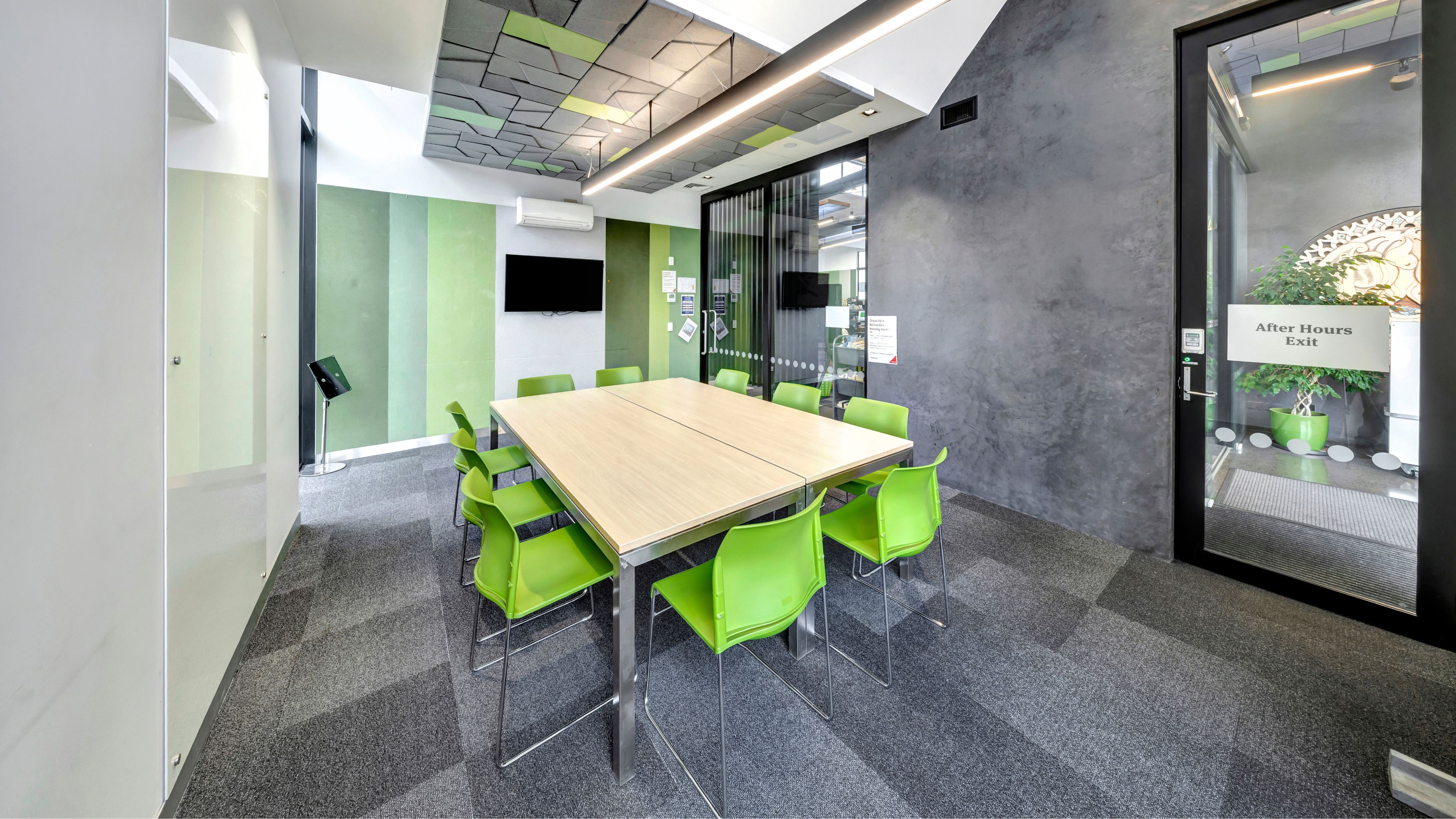 Meeting room with green chairs around a square table, concrete walls, and display screen