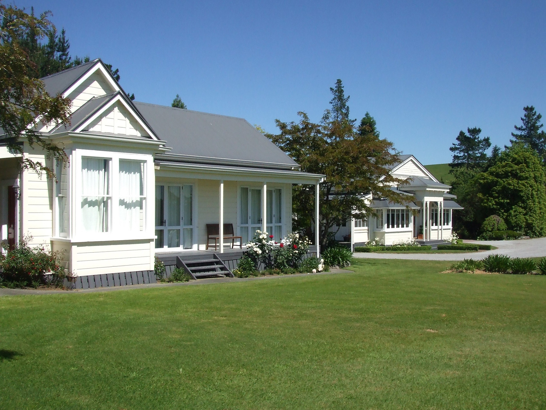 White villa-style buildings with verandas set on a lawn with trees