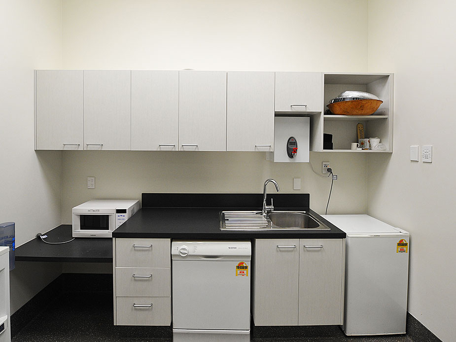 Small kitchenette with white cabinetry, sink, microwave and fridge