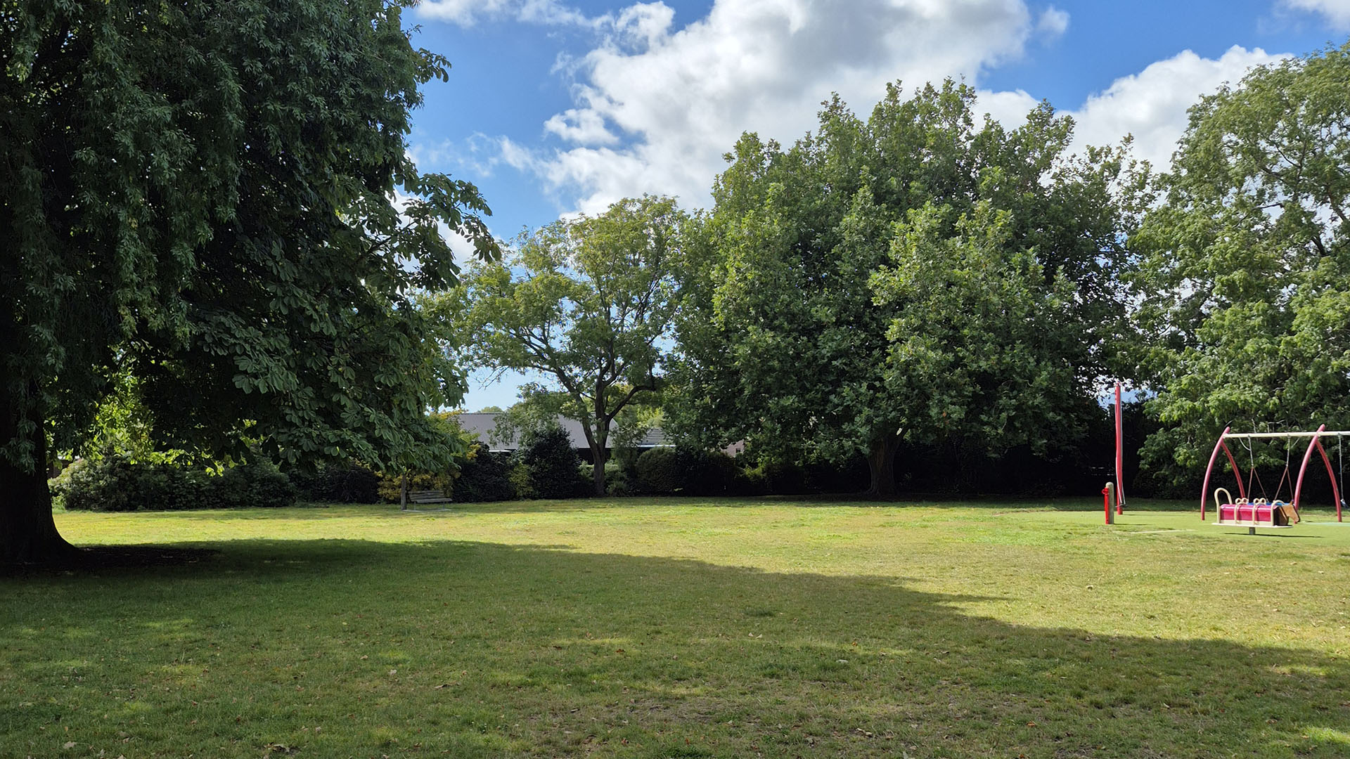 Open grass lawn with playground equipment and mature trees