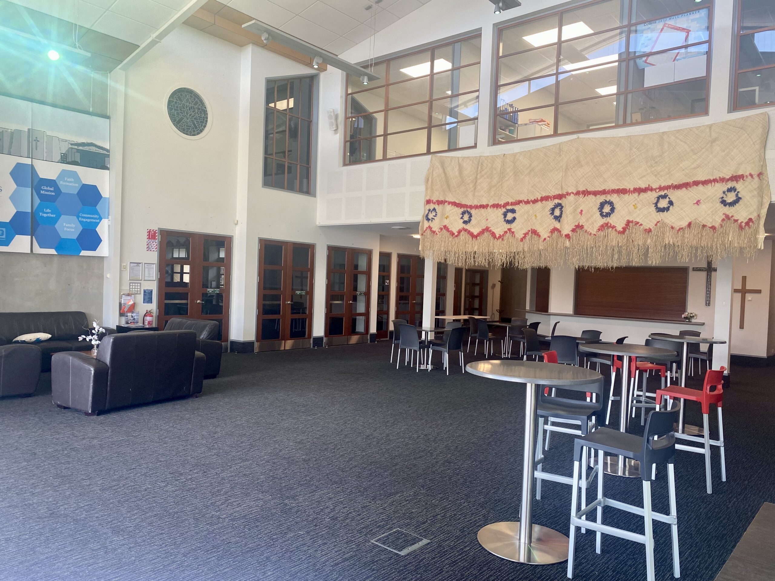 Church foyer with high ceilings, bar-height tables, lounge seating, and decorative textile hanging