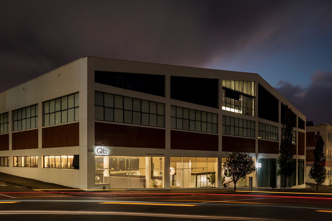 Three-storey brick and white commercial building with large glazed ground floor, night exterior