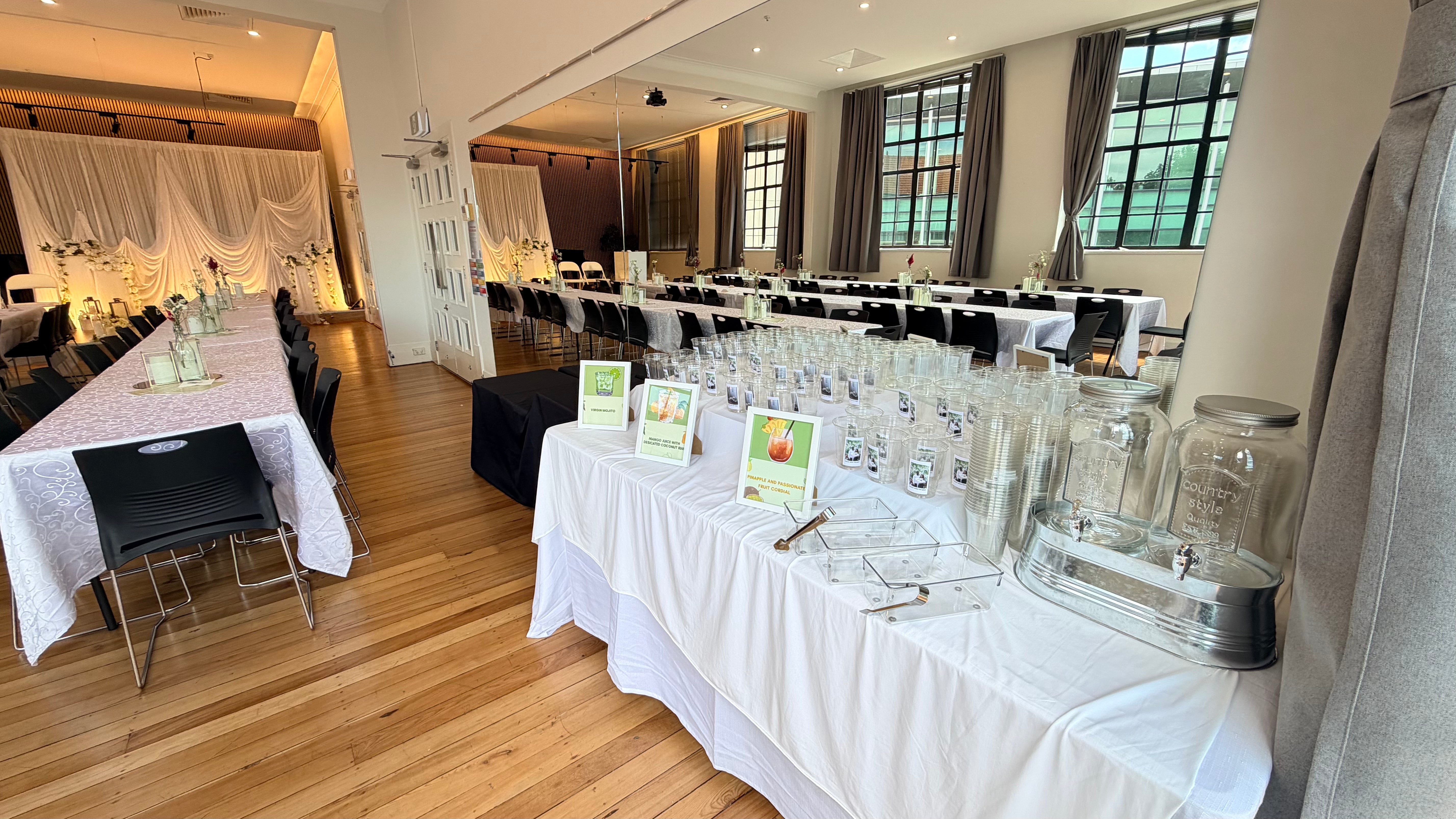 Hall interior with timber floor, round tables dressed in white linen, draped backdrop, and tall windows