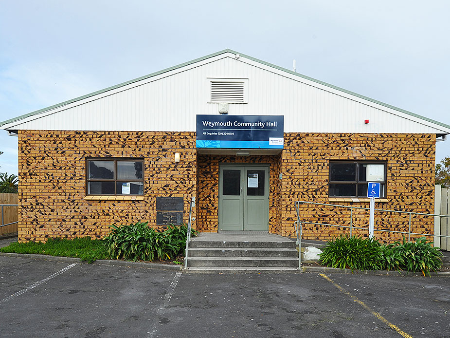 Tan brick hall with gabled white fascia, double green doors, and car park entry