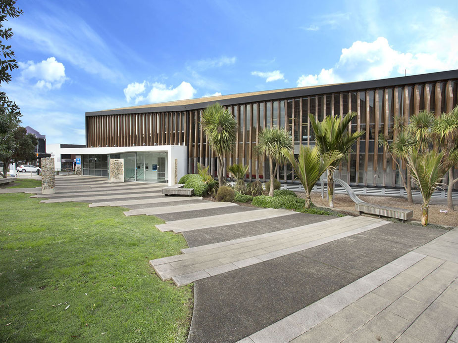 Low-rise contemporary building with horizontal timber louvre cladding, glass entry, and paved approach with planted borders