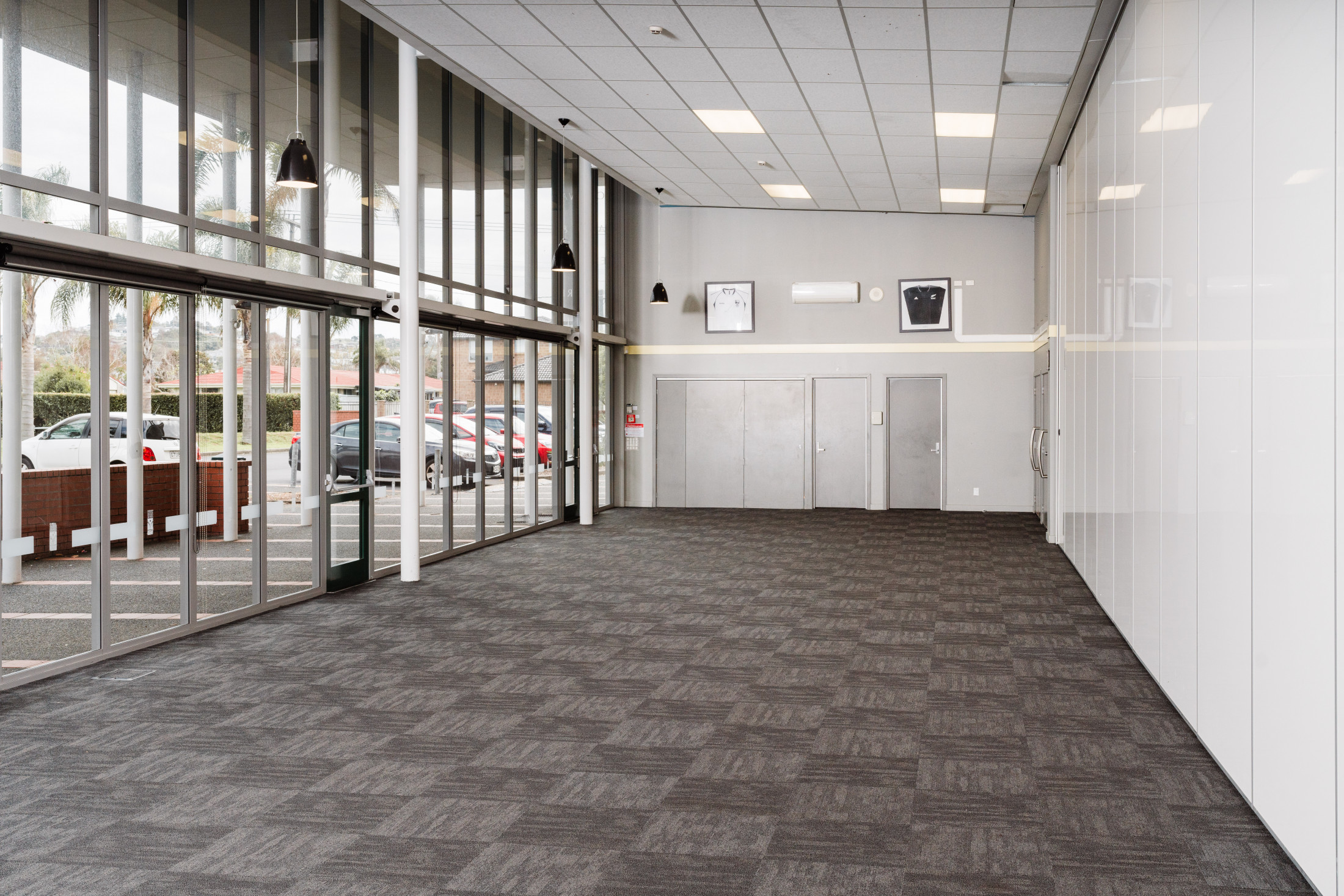 Foyer entrance with full-height glazing, carpet tiles, pendant lights, and open plan layout