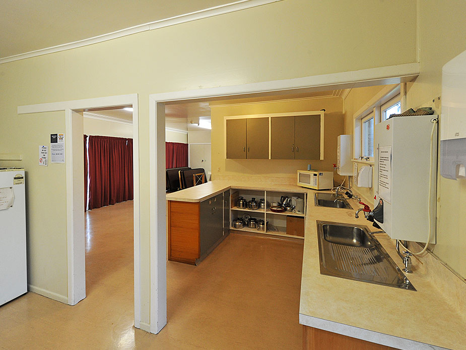 Basic kitchenette area with bench, sink and refrigerator opening to small hall