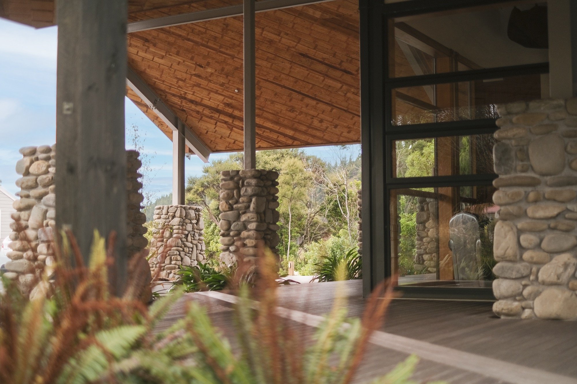 Stone and timber covered entry with stacked-stone columns, timber ceiling, and native planting