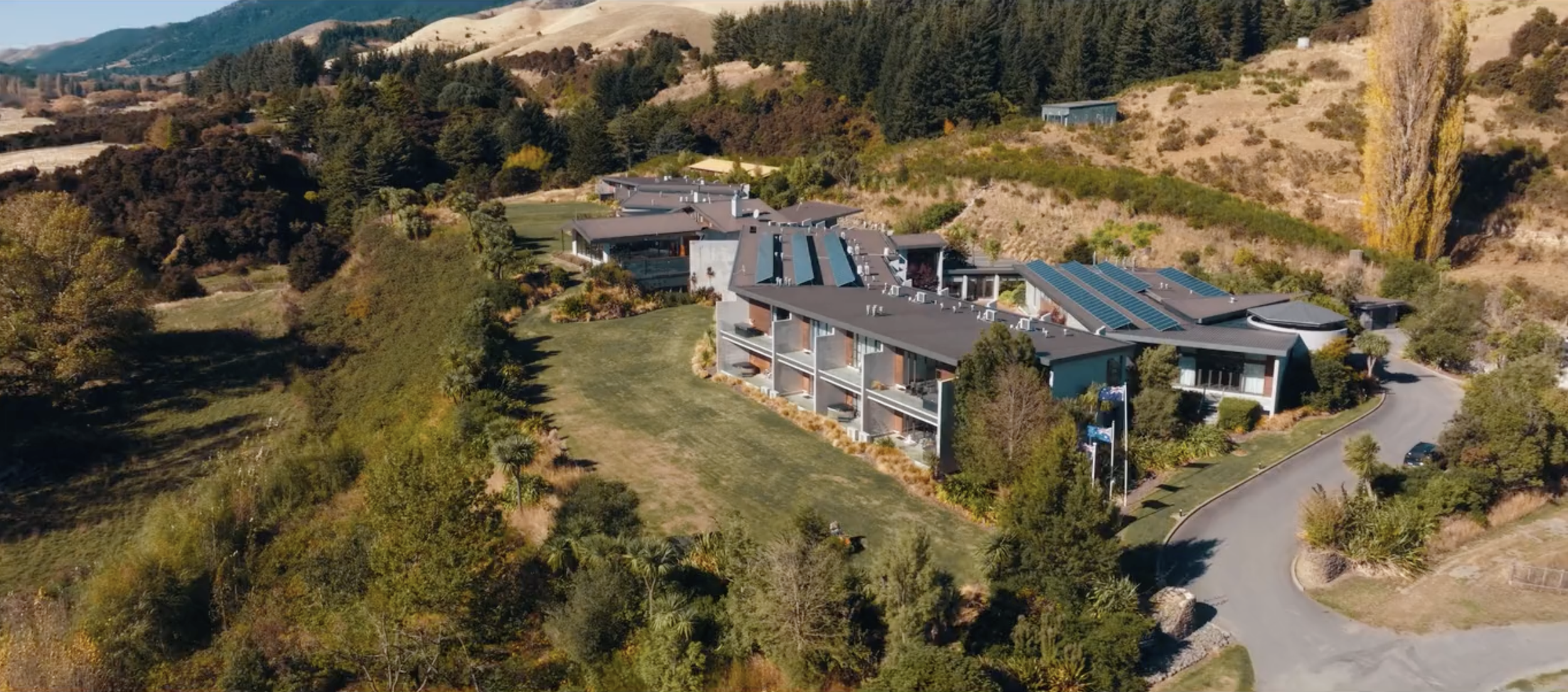 Aerial view of lodge buildings set on green hillside with mountains behind