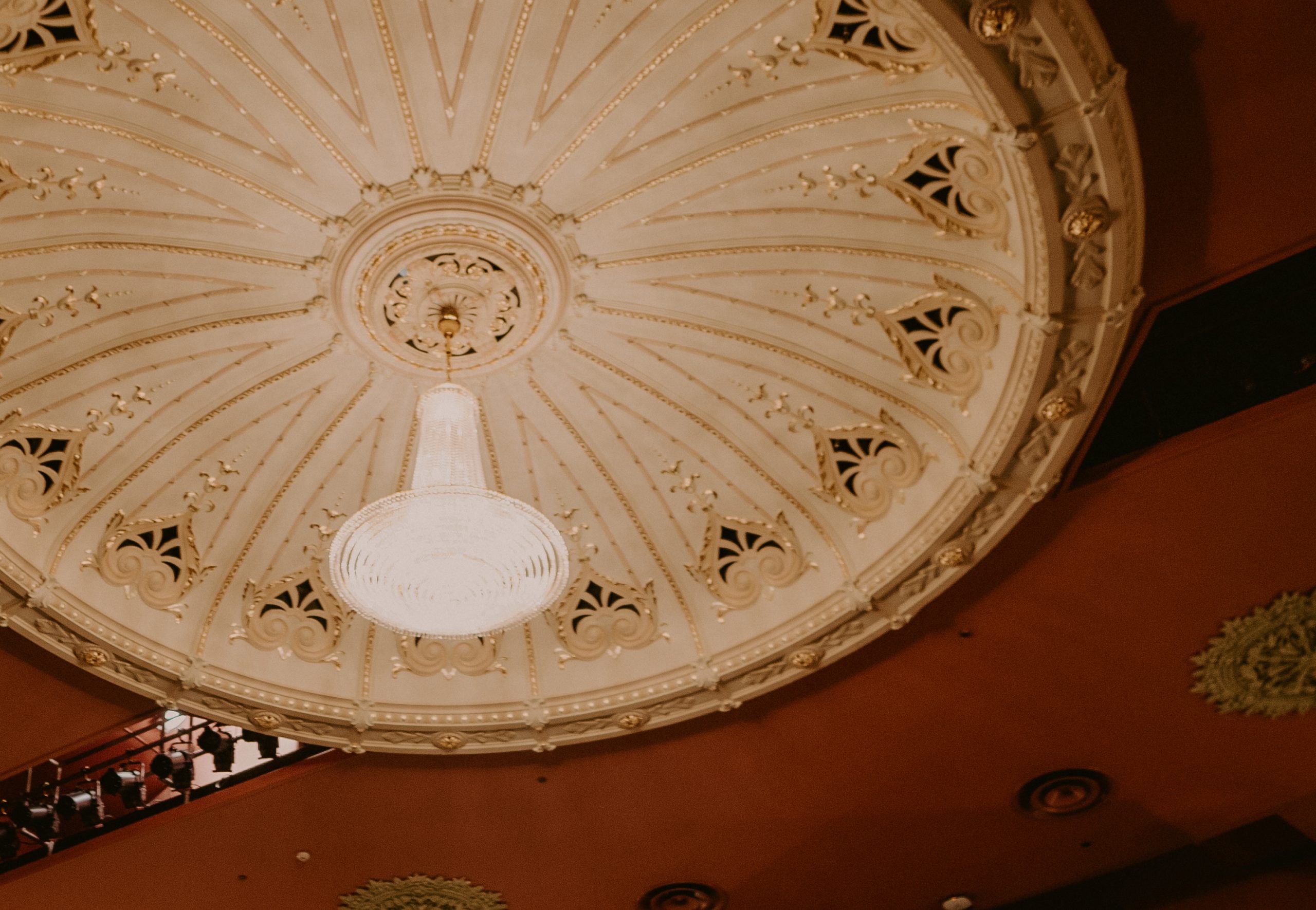 Ornate cream domed ceiling with gold detailing and a central pendant light fixture, terracotta walls