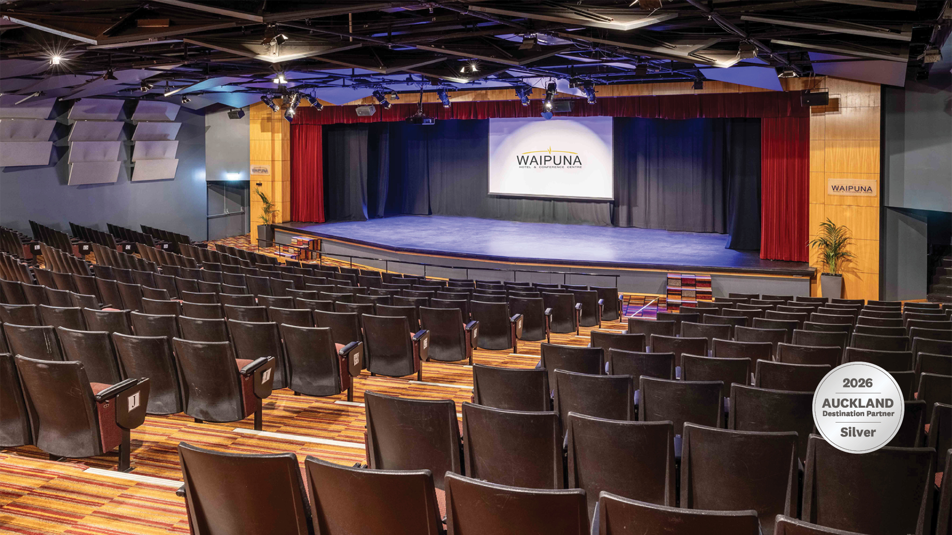 Large tiered auditorium with fixed seating and a raised stage with red curtain