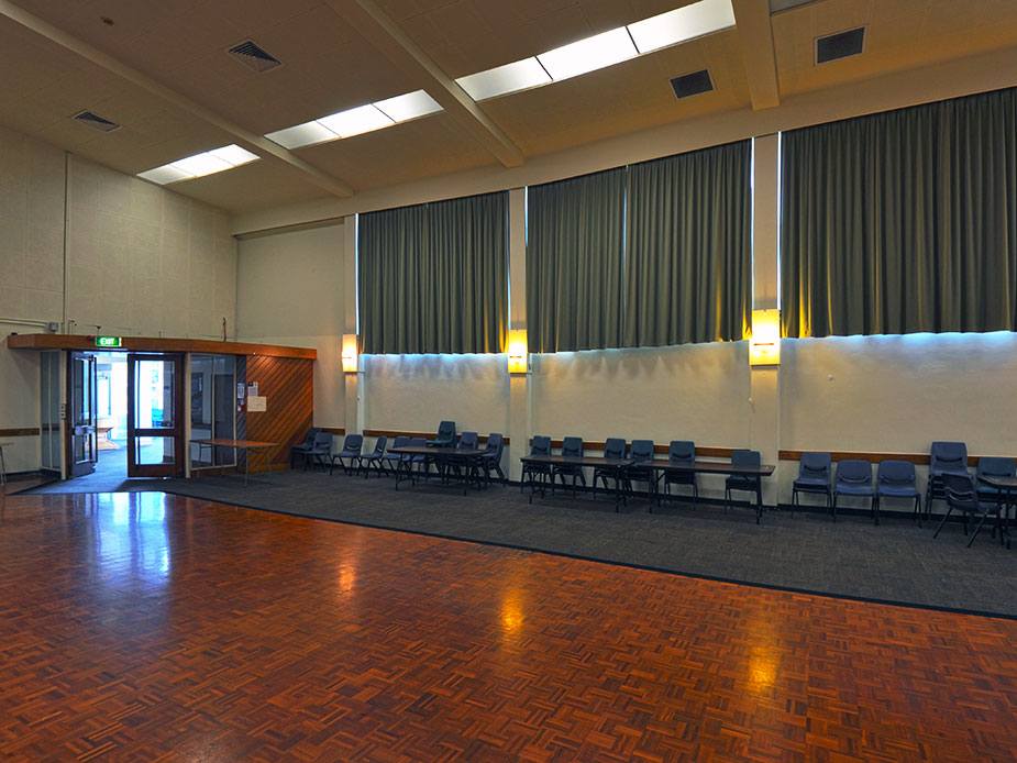 Large hall with parquet floor, grey curtains and rows of chairs along wall