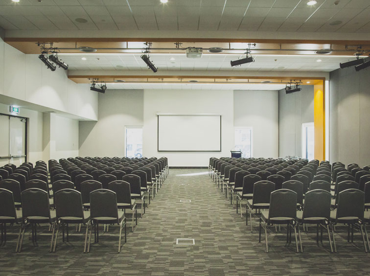 Large conference hall with rows of chairs and projection screen at front