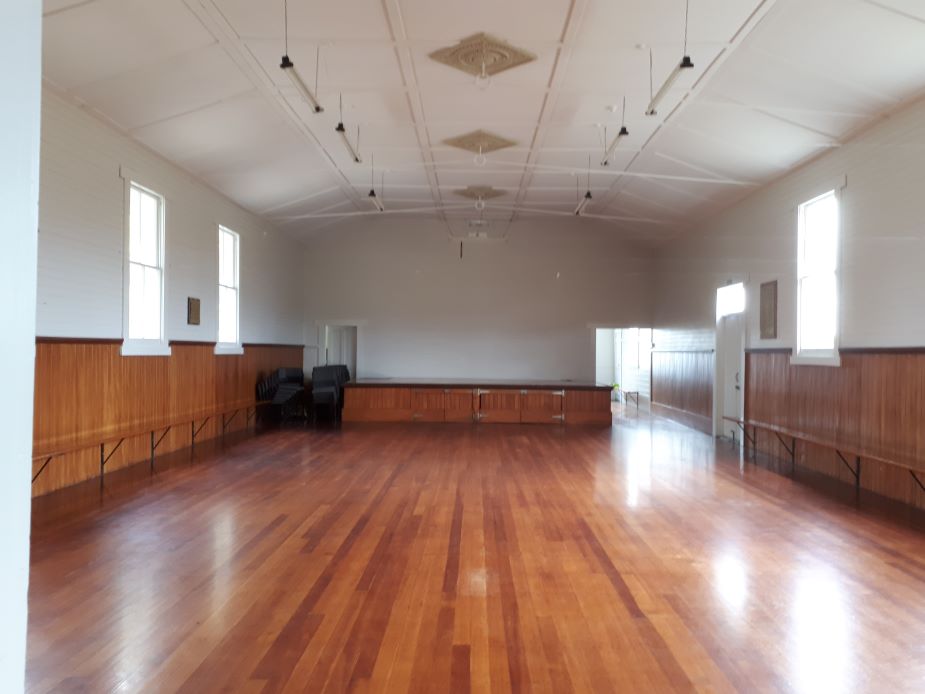 Empty white hall with polished timber floor, timber wainscoting, arched ceiling, and raised platform