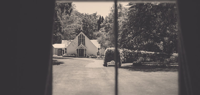 View through window frames of a white chapel across a manicured lawn