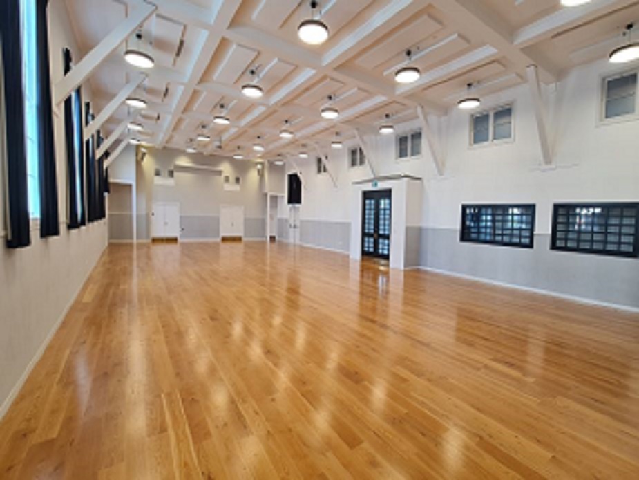 Large empty hall with timber floor, beamed ceiling, and professional lighting