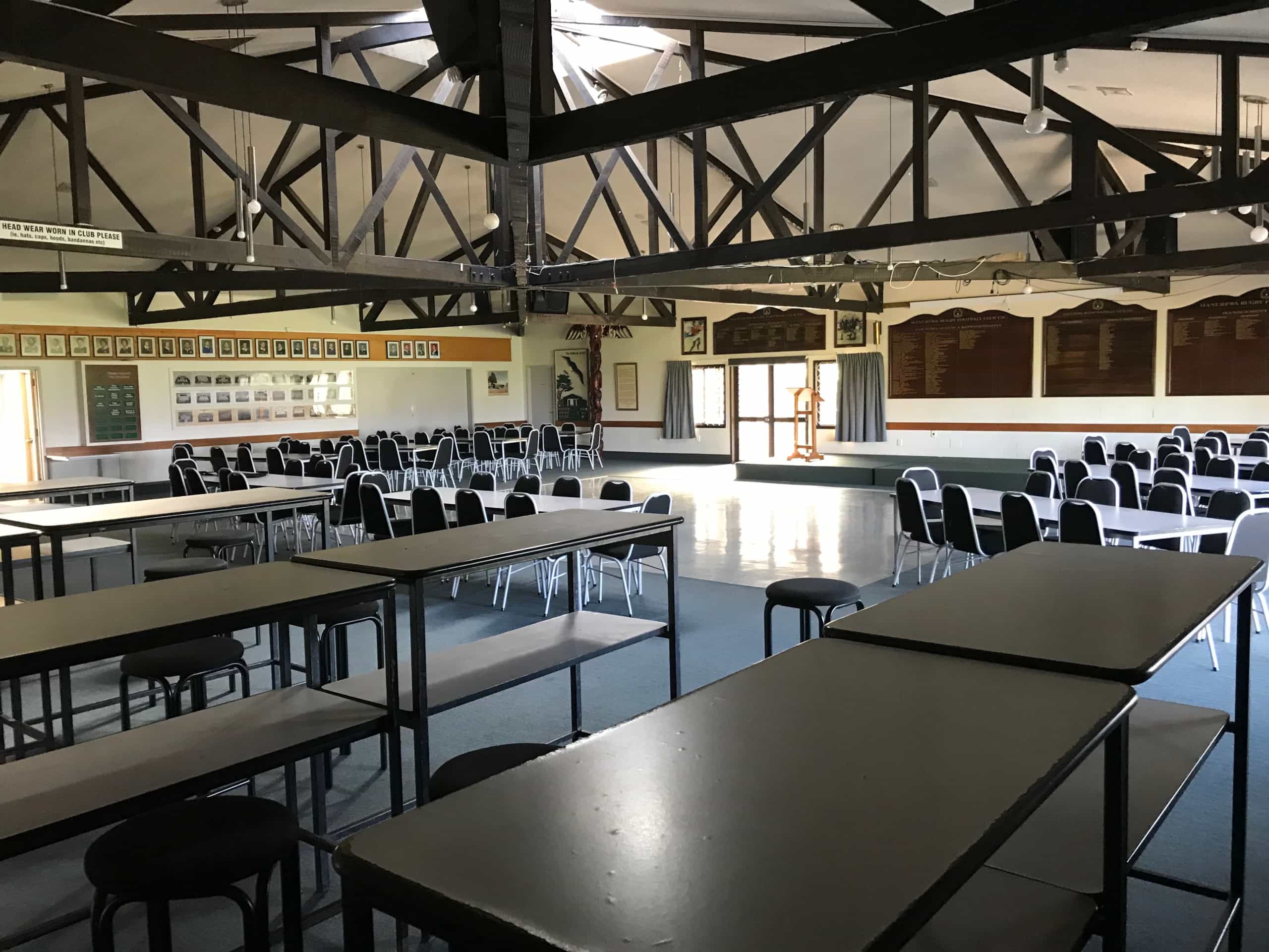 Large club hall with exposed dark timber roof trusses, tables, and club memorabilia on walls