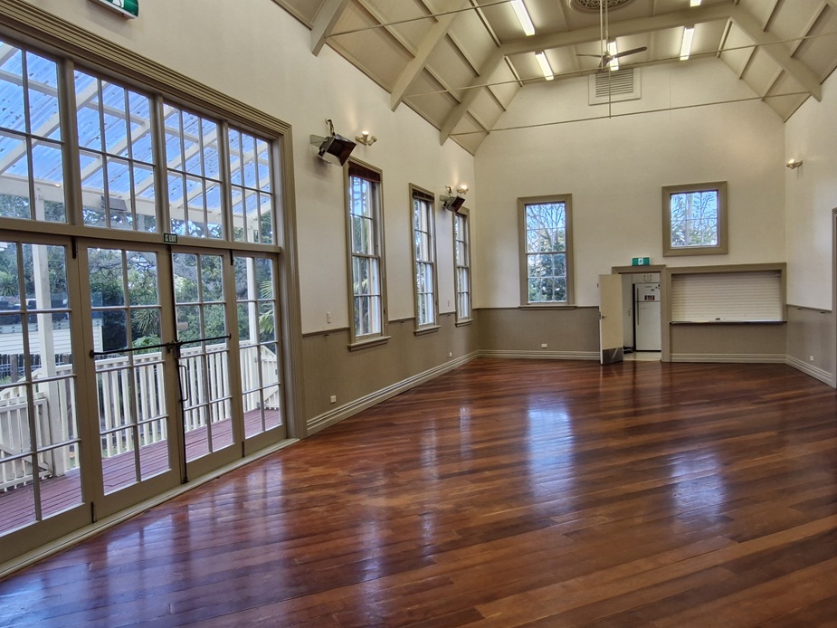 Timber-floored hall with high vaulted ceiling, exposed rafters, tall windows and verandah doors