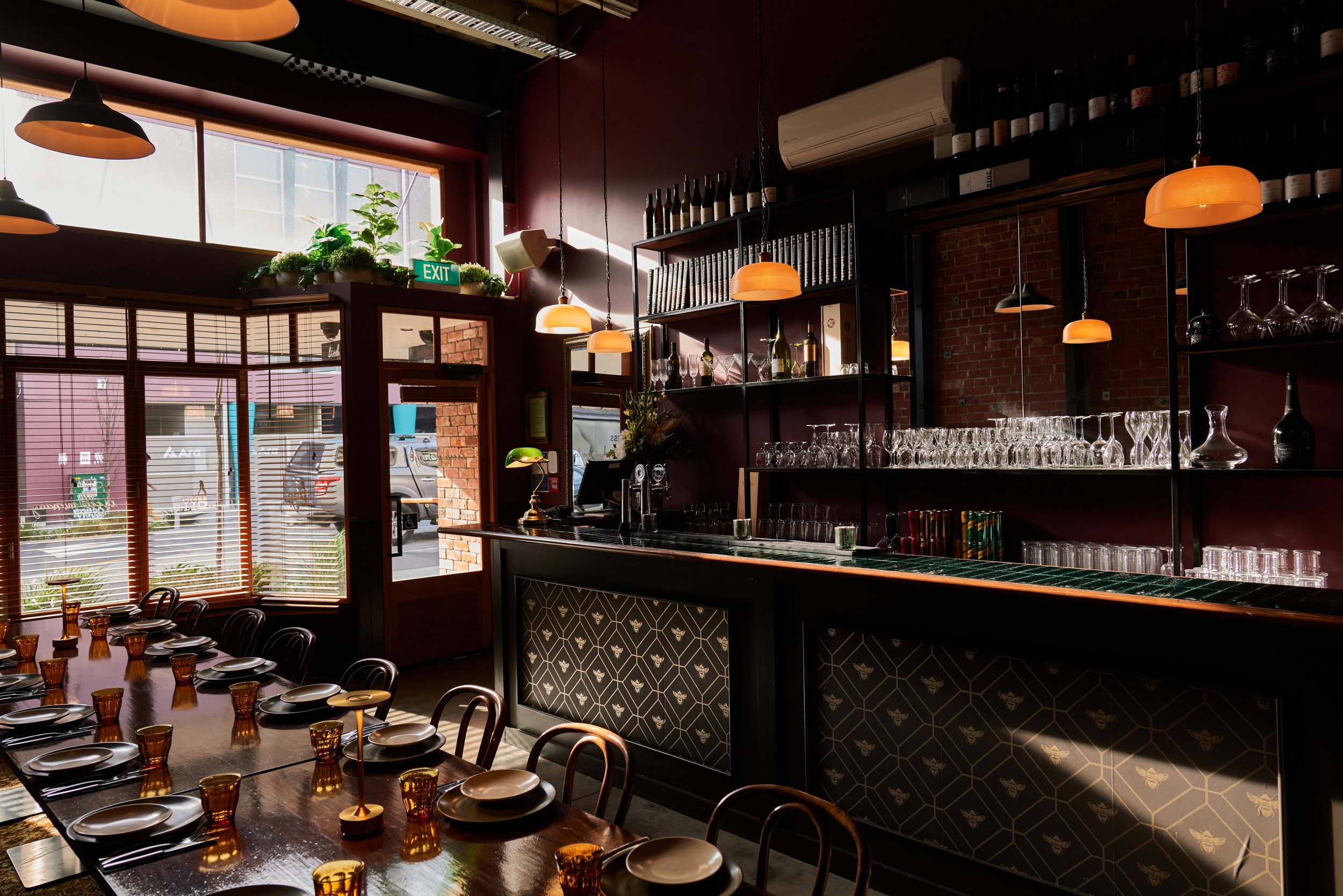 Deep red-walled dining room with patterned tile bar front, amber pendant lights and long table setting