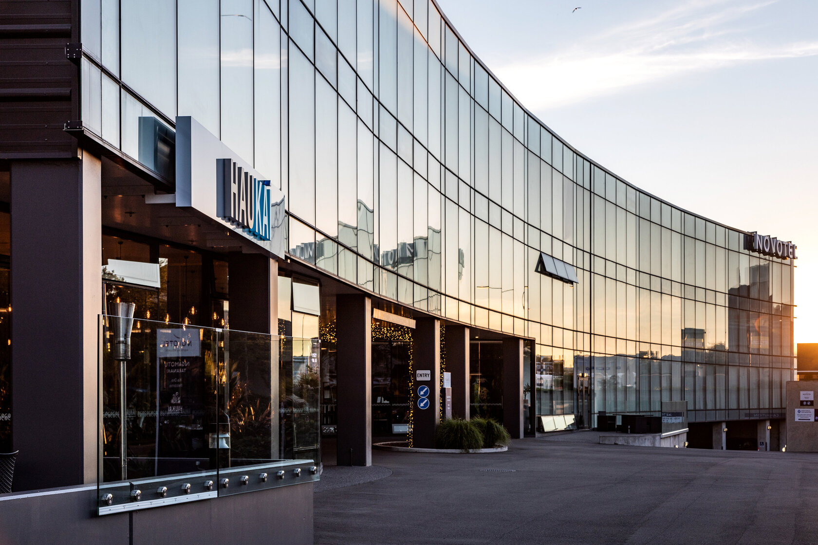 Curved glass-facade building exterior with dark columns and signage at sunset