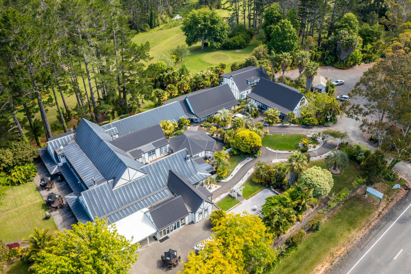 Aerial view of lodge complex with pitched roofs surrounded by mature gardens