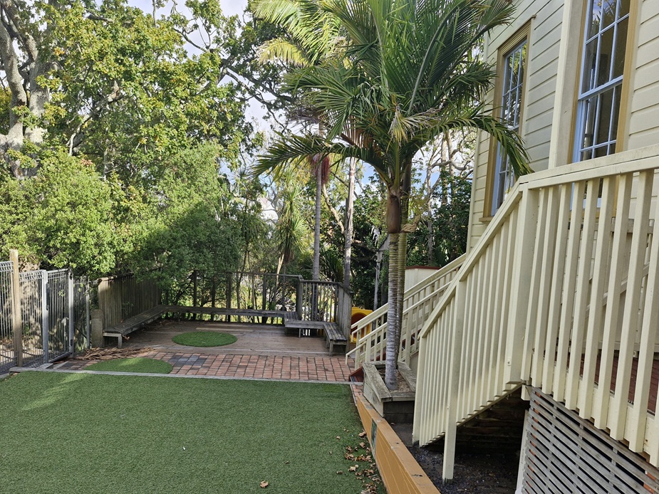 Outdoor courtyard with lawn, raised timber deck, stairs and surrounding trees