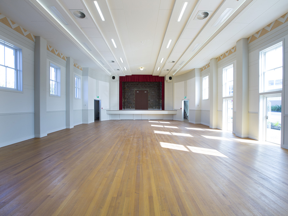 Renovated hall interior with polished timber floor, raised platform with red curtain, and decorative ceiling