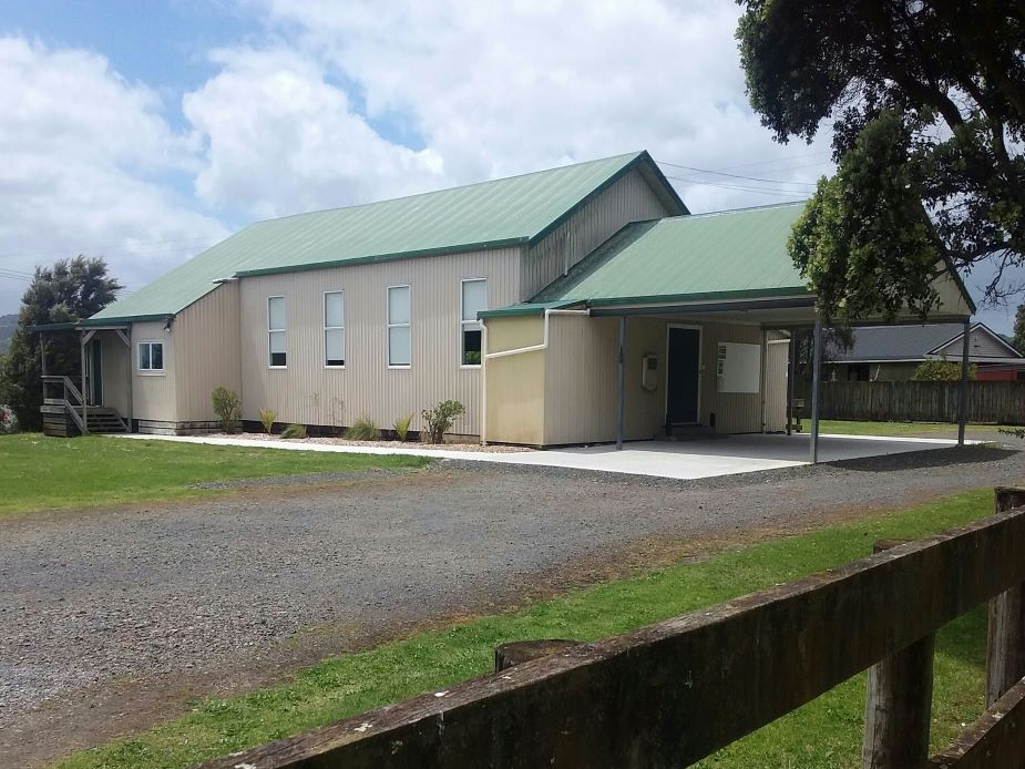 Single-storey metal-clad hall with green corrugated roof, covered entry, gravel forecourt