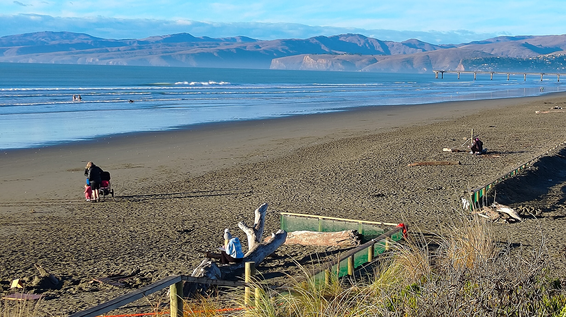 Sandy beach with hills in the background and people walking along the shore