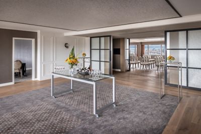 Hotel suite with lounge area, glass partition, and dining area beyond