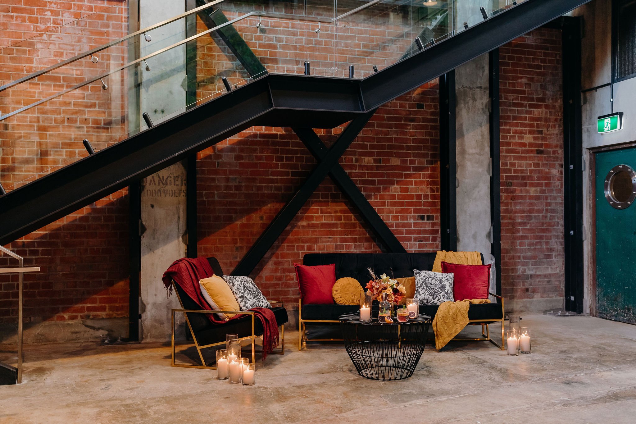 Lounge seating area with velvet sofas and candles beside exposed brick wall and steel staircase