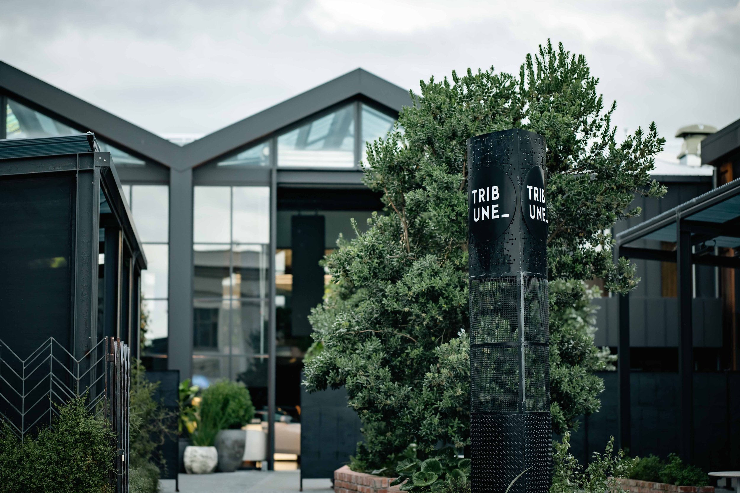 Dark-clad venue exterior with peaked gable glazing and branding signpost