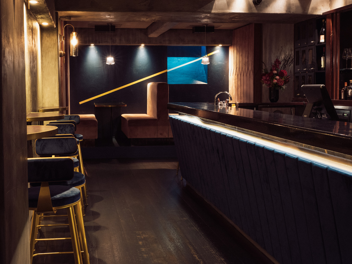 Dark intimate bar with navy velvet stools, lit bar counter, and pink booth seating