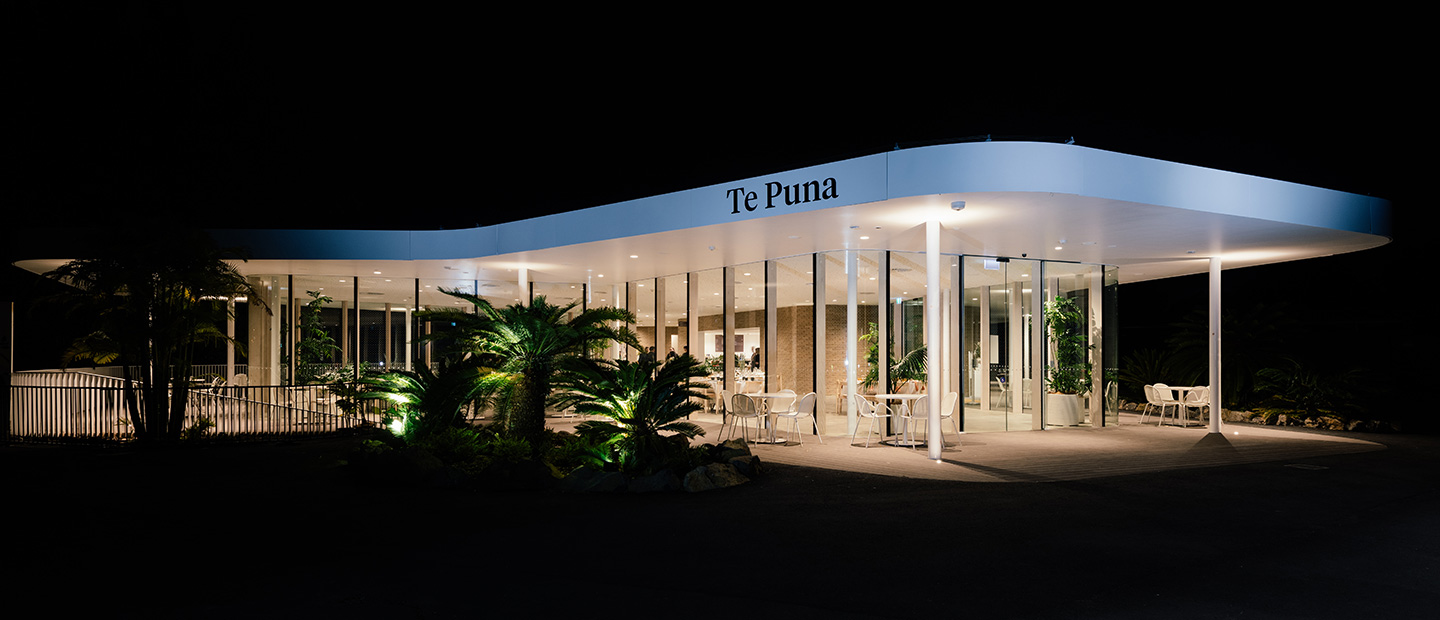 Modern curved building exterior illuminated at night with landscaping