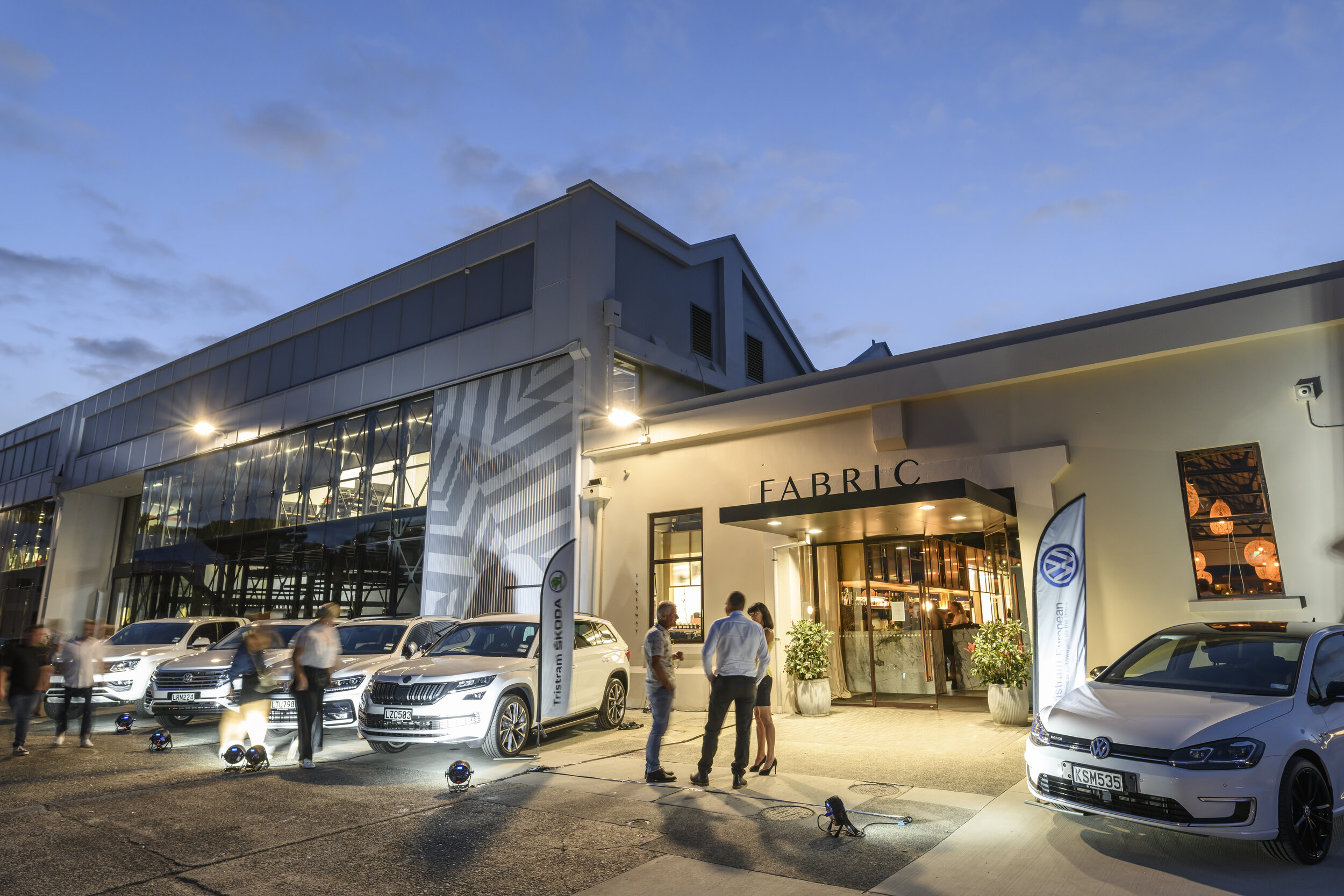 White rendered commercial building exterior at dusk with illuminated entrance and vehicles outside