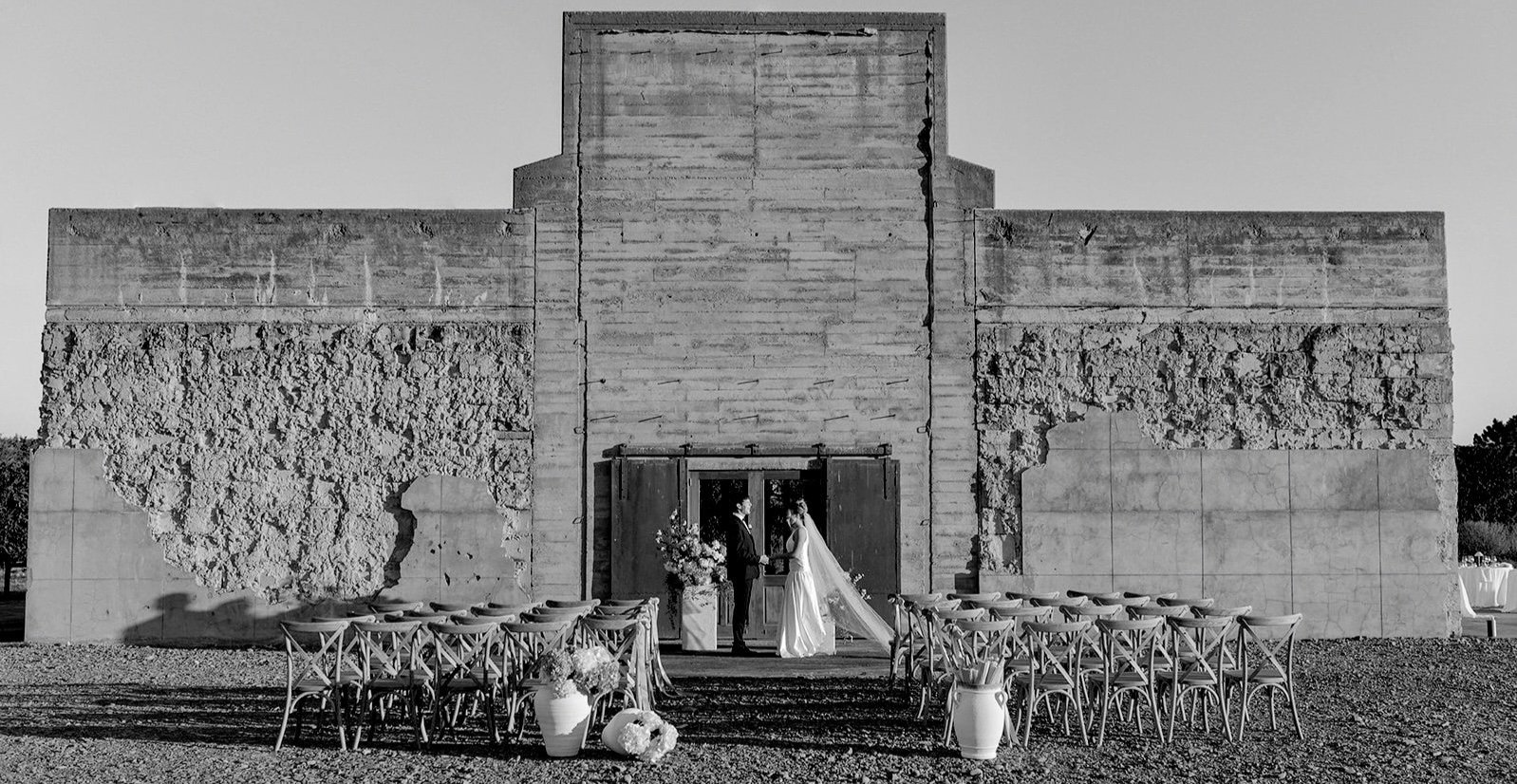 Rough concrete block building with stepped facade, rows of chairs set for outdoor ceremony