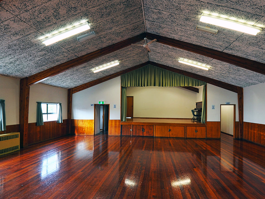 Hall interior with timber-beamed gable ceiling, polished floor, and raised platform with curtain