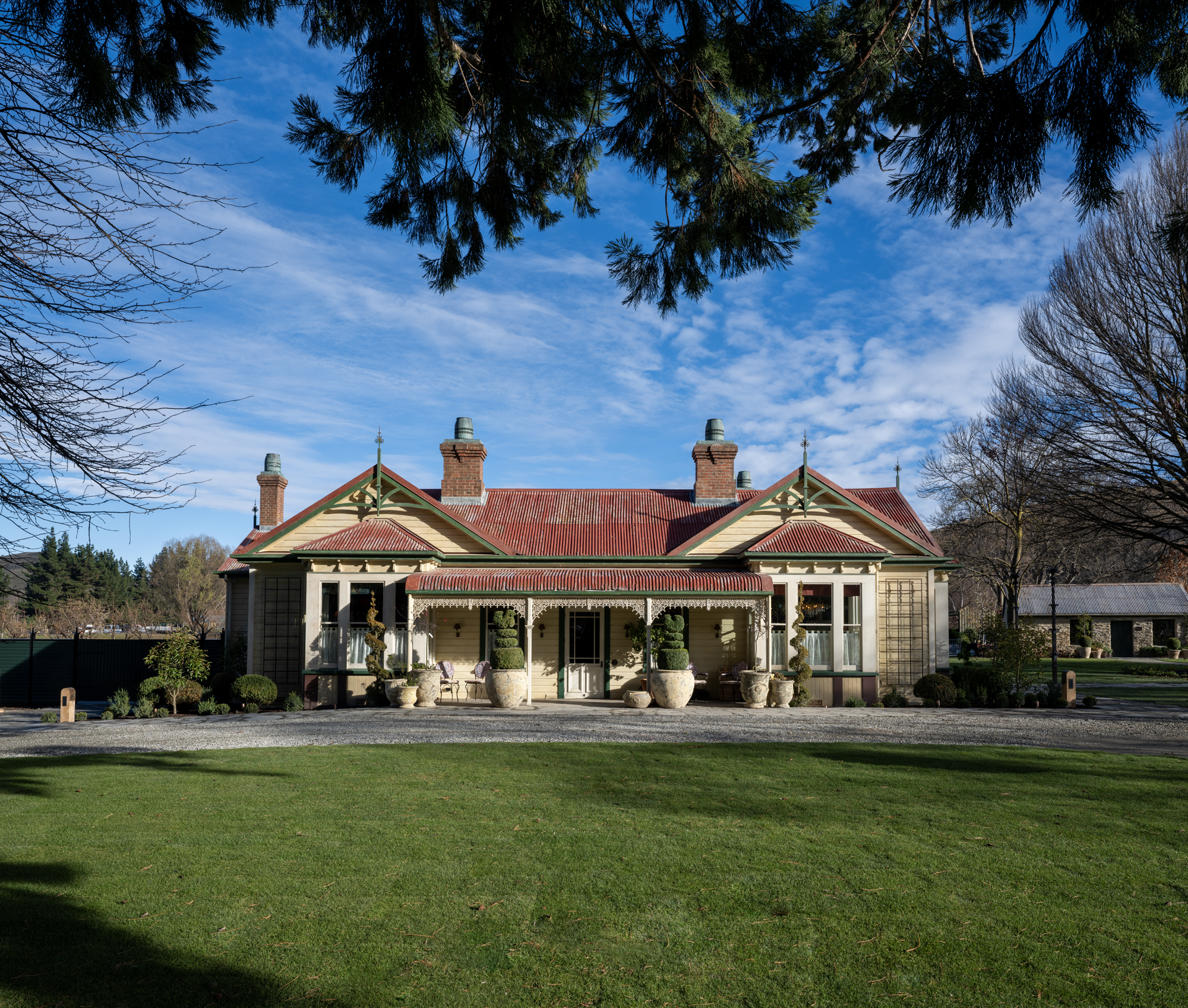 Victorian homestead building at Ayrburn with ornate verandah, topiary urns, and open lawn in foreground