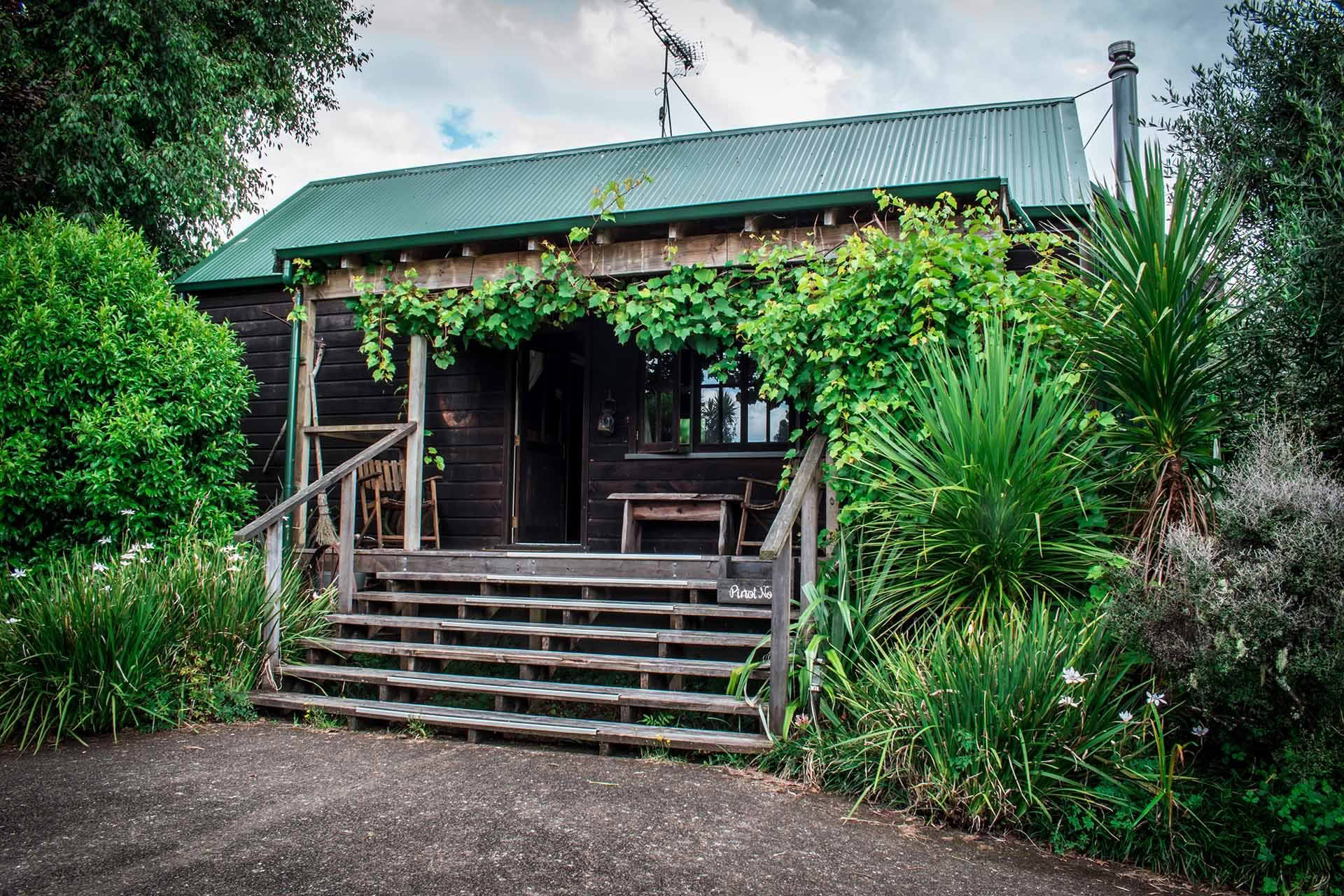 Dark timber cottage with covered verandah surrounded by lush garden