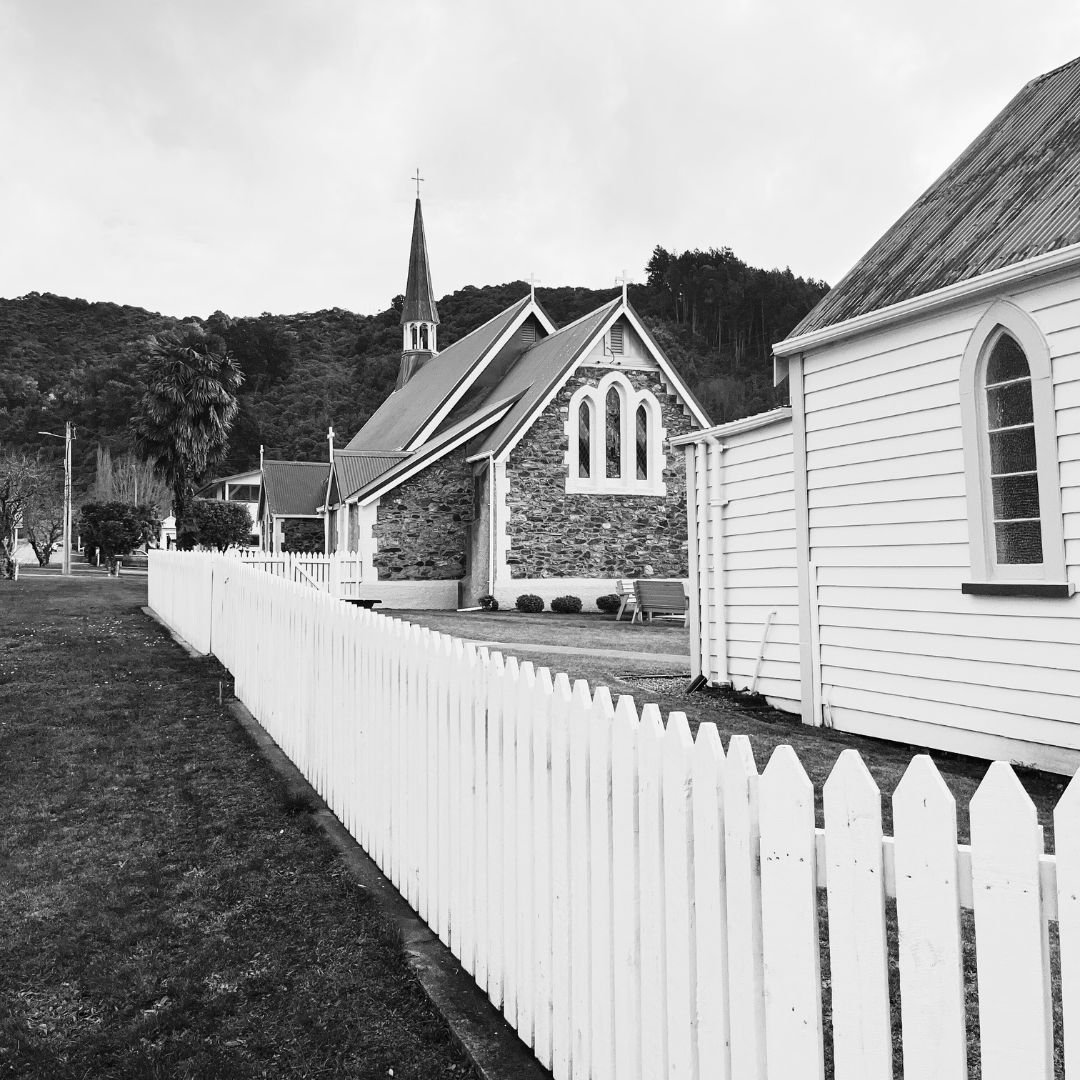 Black and white view of stone church buildings with white picket fence