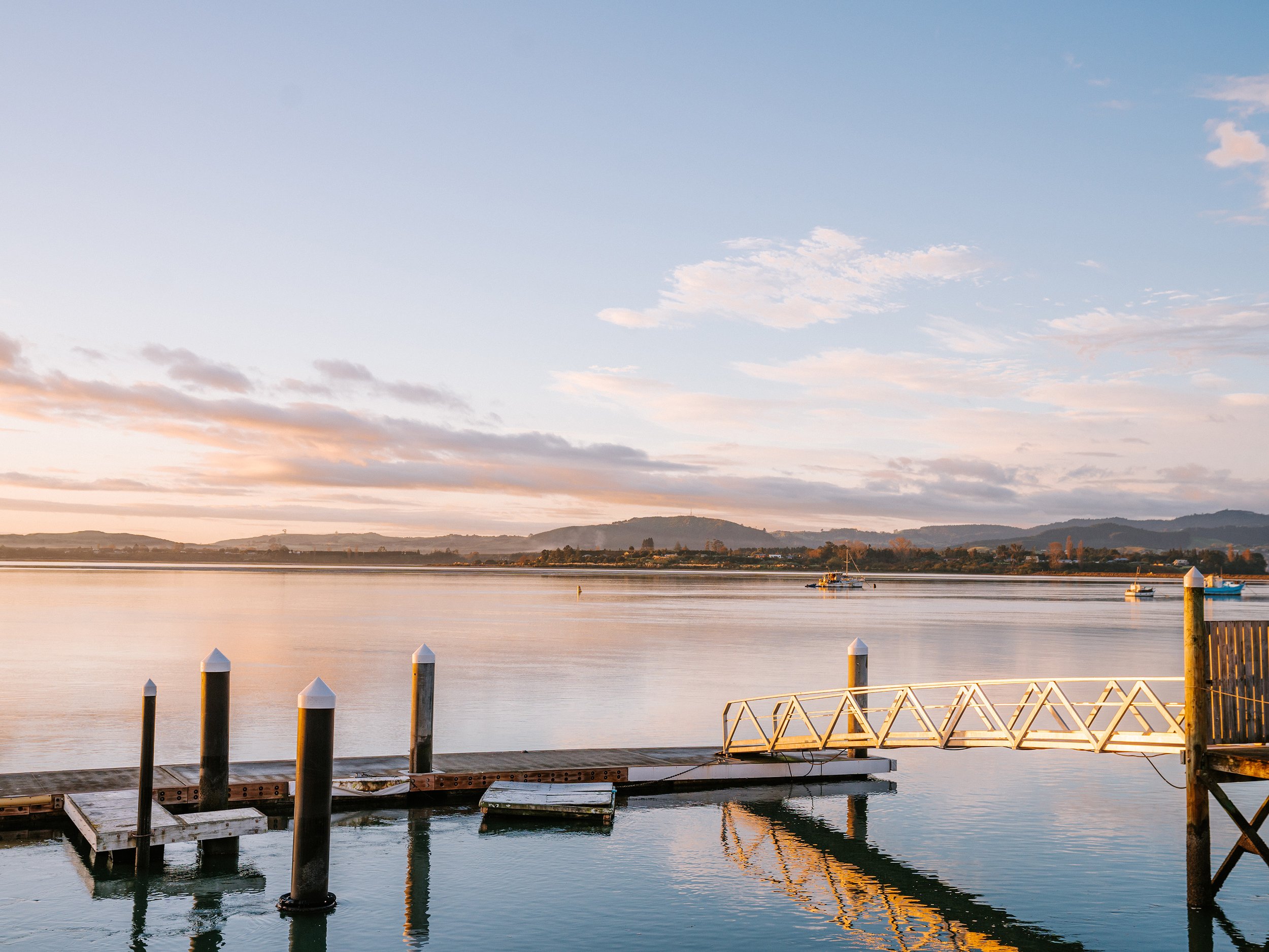 Waterfront jetty with bollard posts and lit gangway at calm sunrise, hills beyond