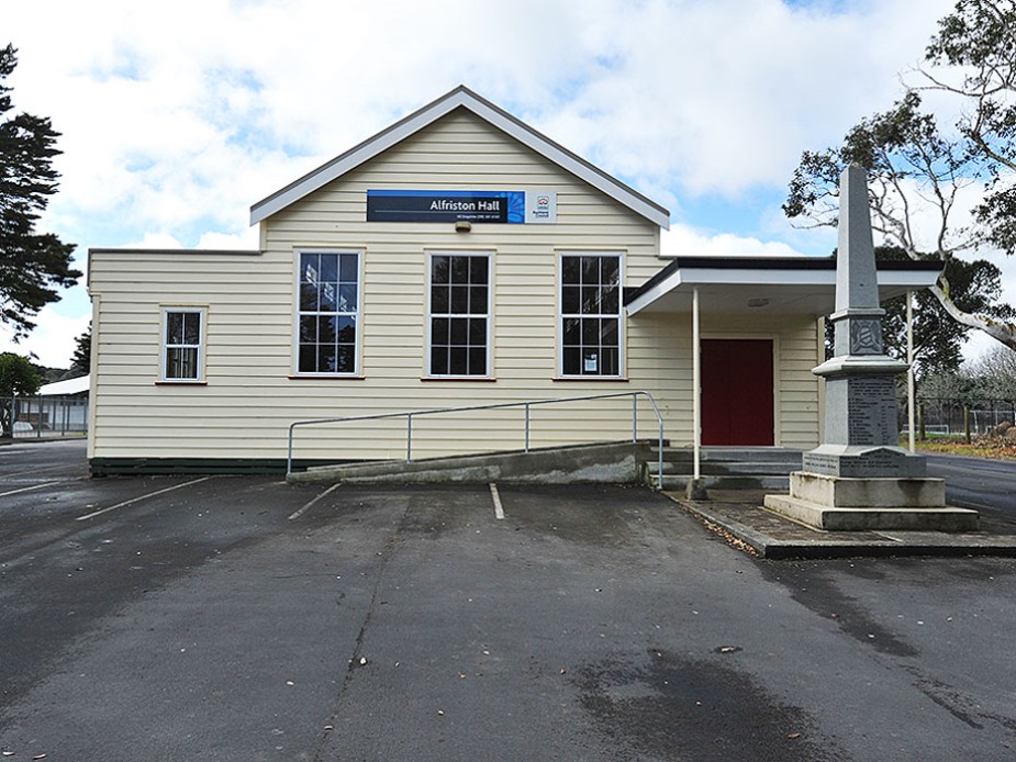 Cream weatherboard hall with red door and war memorial beside car park