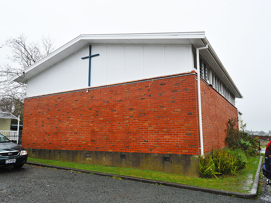 Brick hall exterior with cross mounted on white upper gable
