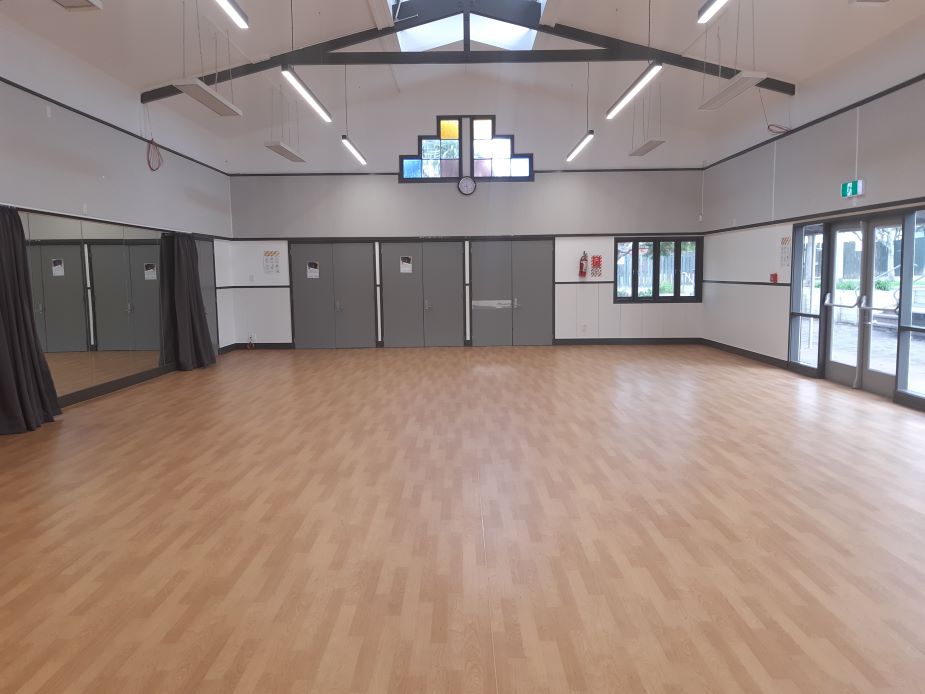 Plain rectangular hall with timber floor and vaulted ceiling with stained glass accent