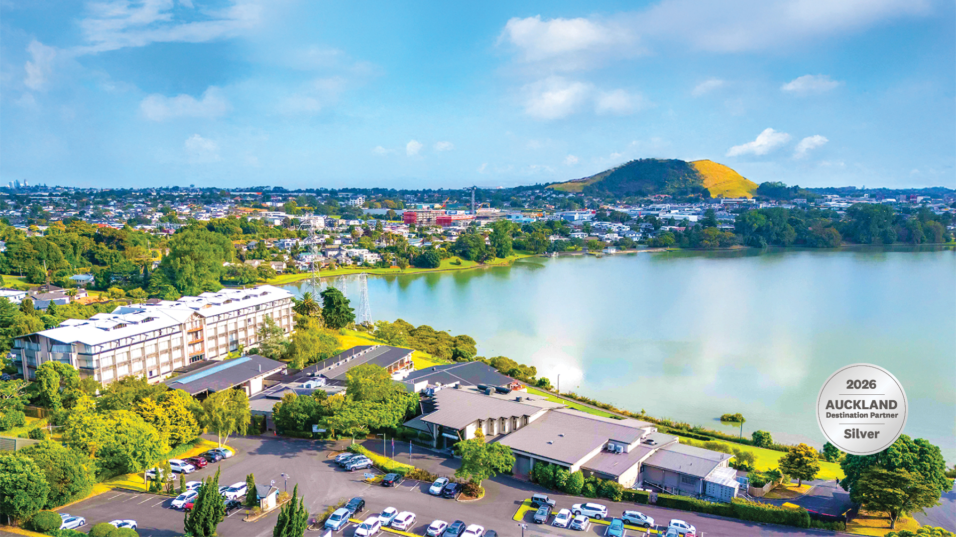 Aerial view of hotel buildings beside a lake with a volcanic hill beyond