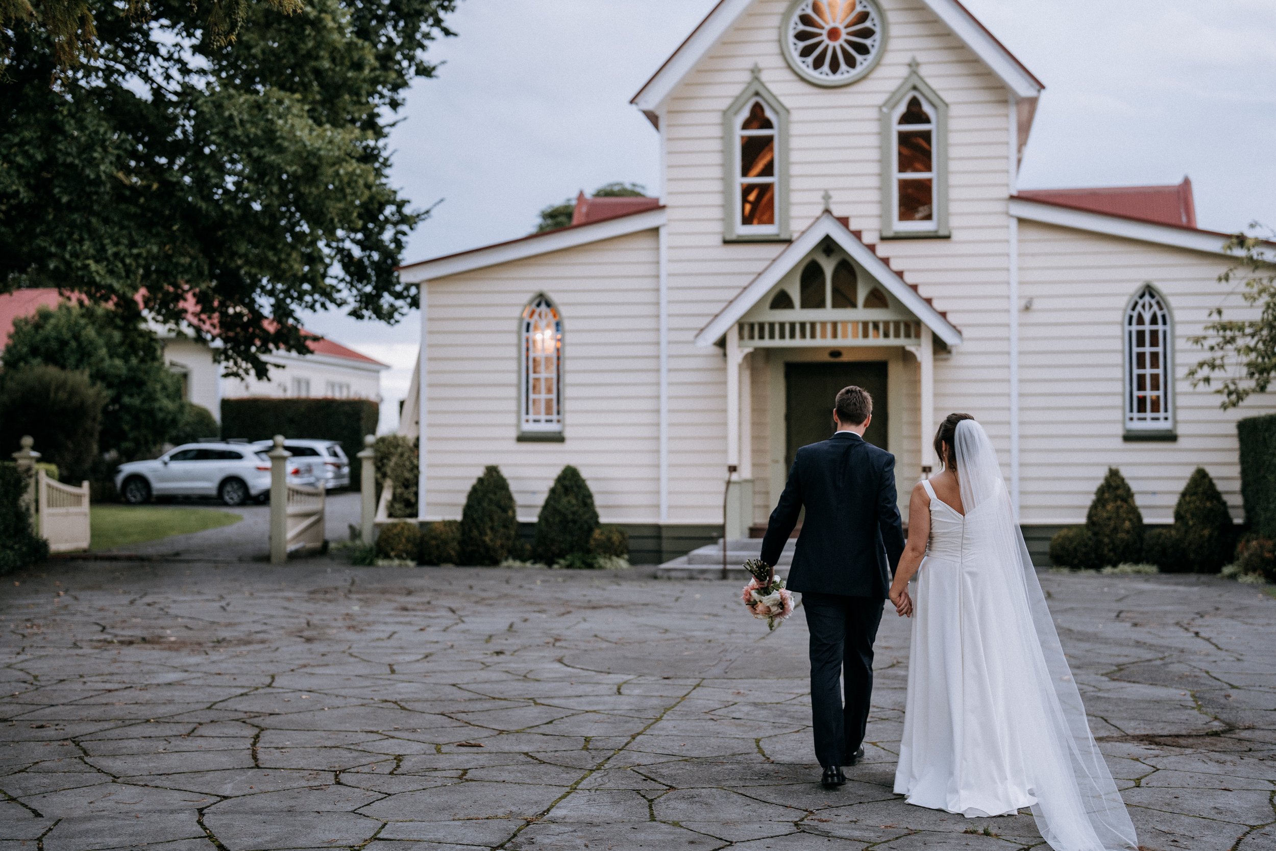 White timber church with gothic arched windows and red roof on paved forecourt