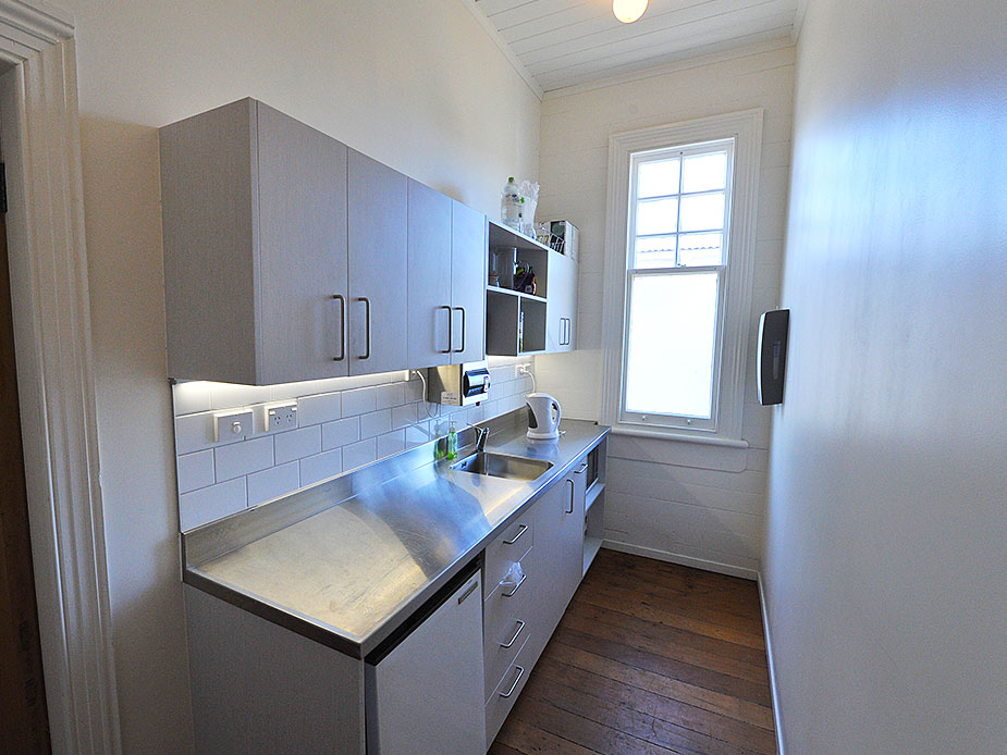 Compact galley kitchen with grey cabinets and stainless bench in heritage room