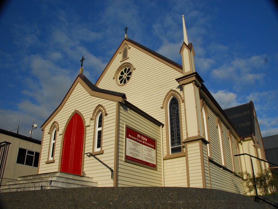Timber-clad church exterior with steeple, arched windows and red door